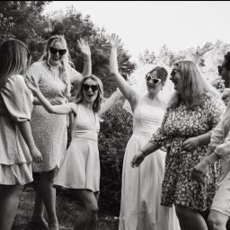 CloudPhotography - Czarno-białe zdjęcie grupy roześmianych kobiet w okularach przeciwsłonecznych, unoszących ręce w górę, na tle zieleni. Jedna z nich ma welon.