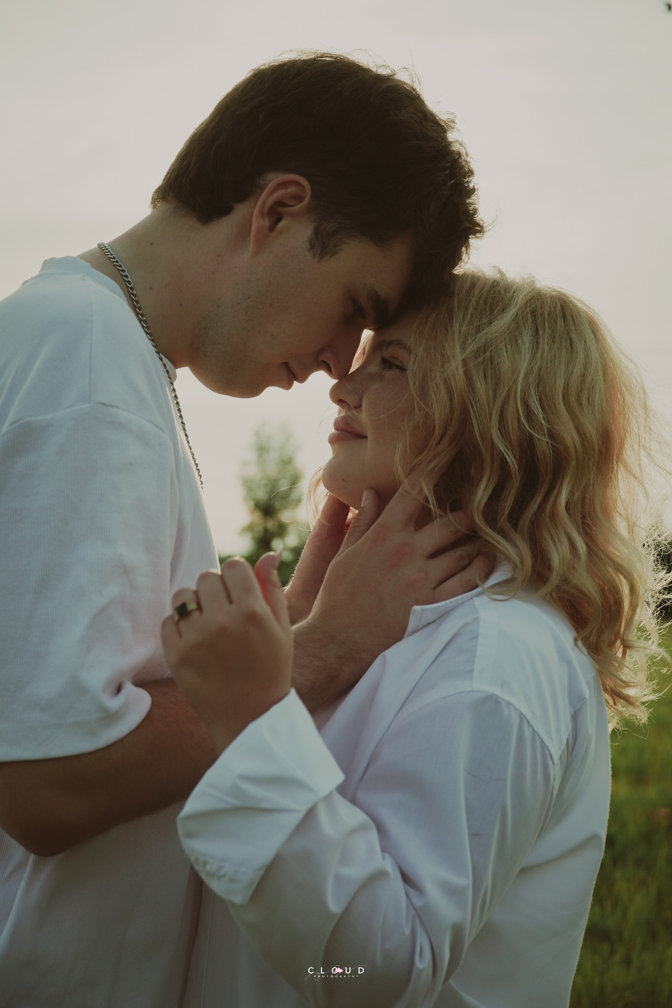 Romantyczna sesja narzeczeńska w plenerze: para w białych koszulach, delikatny dotyk, ciepłe światło zachodzącego słońca, subtelny uśmiech.