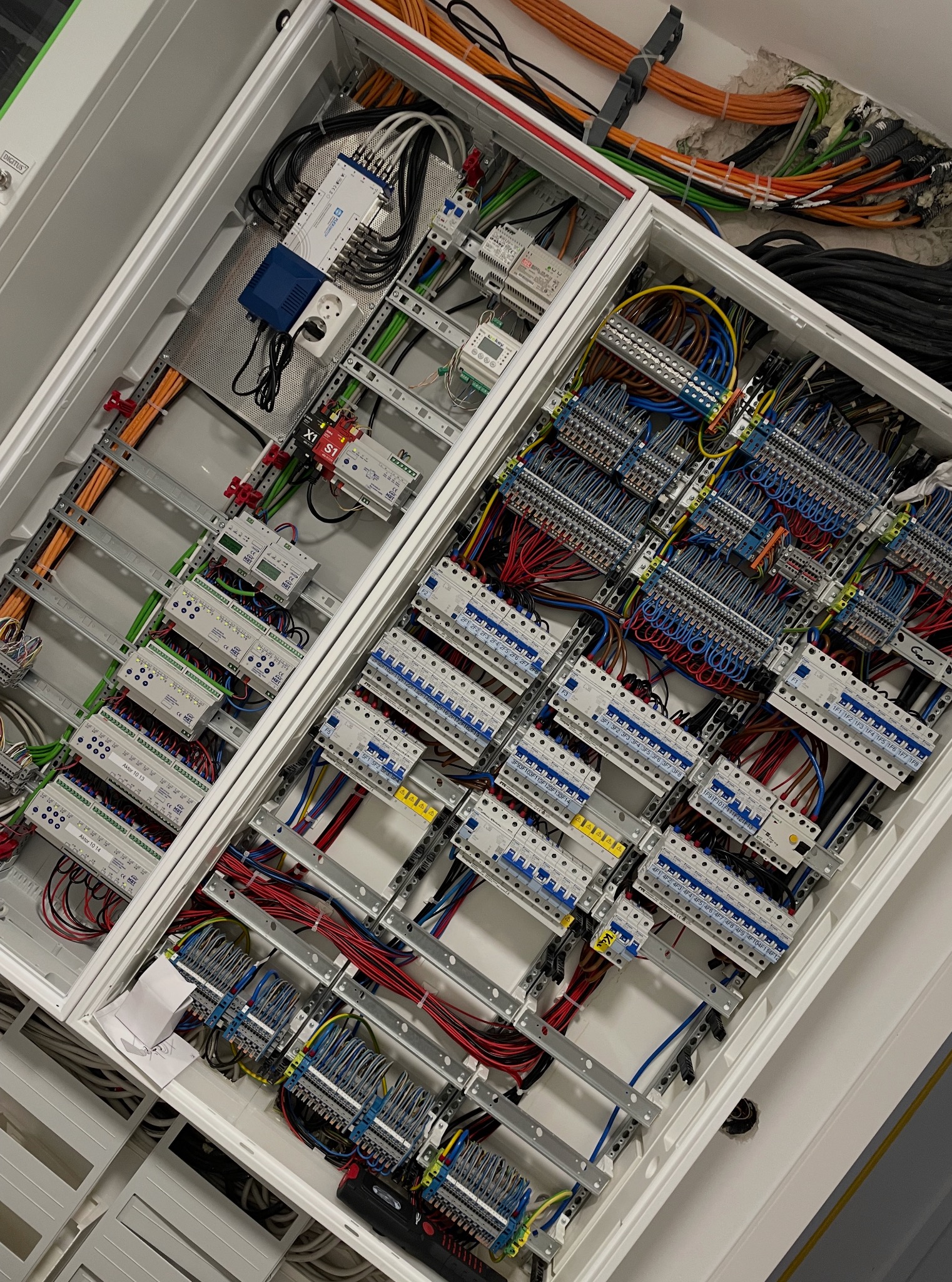 Rozdzielnia elektryczna w białej obudowie, widok z góry. Liczne kable, bezpieczniki i moduły sterujące. Uporządkowany układ przewodów wewnątrz.