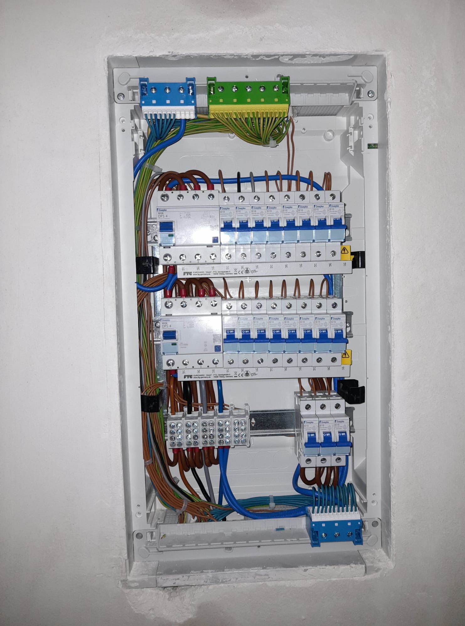 Rozdzielnia elektryczna wnękowa z zabezpieczeniami różnicowoprądowymi i nadprądowymi, z widocznymi przewodami w izolacji brązowej, niebieskiej i zielono-żółtej.