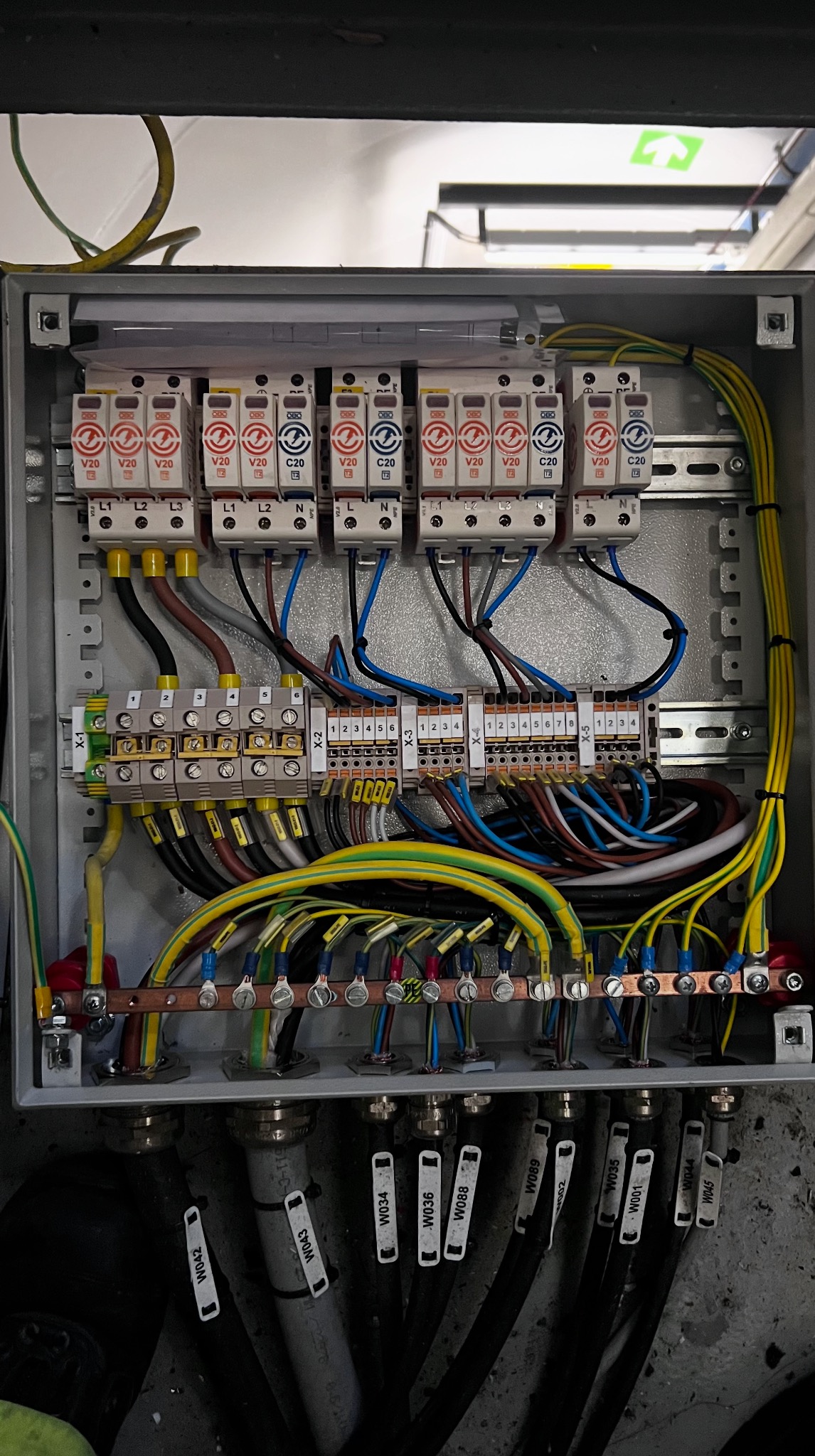 Otwarta skrzynka elektryczna z bezpiecznikami i okablowaniem. Widoczne liczne przewody w różnych kolorach oraz oznaczenia na kablach. Instalacja wygląda na nową i uporządkowaną.