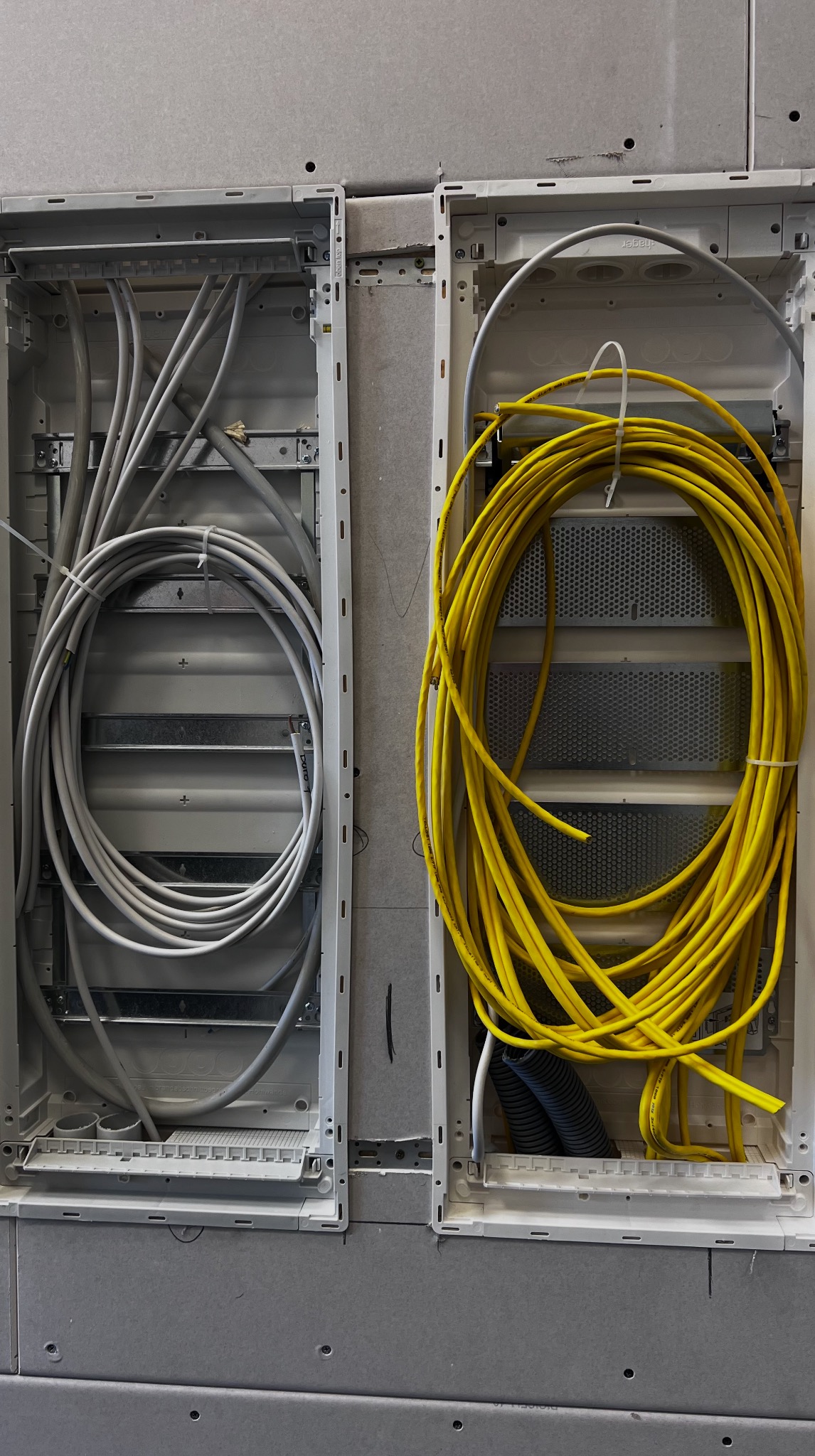 Dwa panele z kablami: szare w lewym, zwinięte żółte w prawym. Widok z bliska na kable ułożone w panelach w ścianie gipsowo-kartonowej.