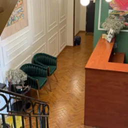 Eleganckie wnętrze biura z recepcją, zielonymi fotelami i parkietem w jodełkę. W tle dekoracje ścienne i oświetlenie. Widok z góry na hol.