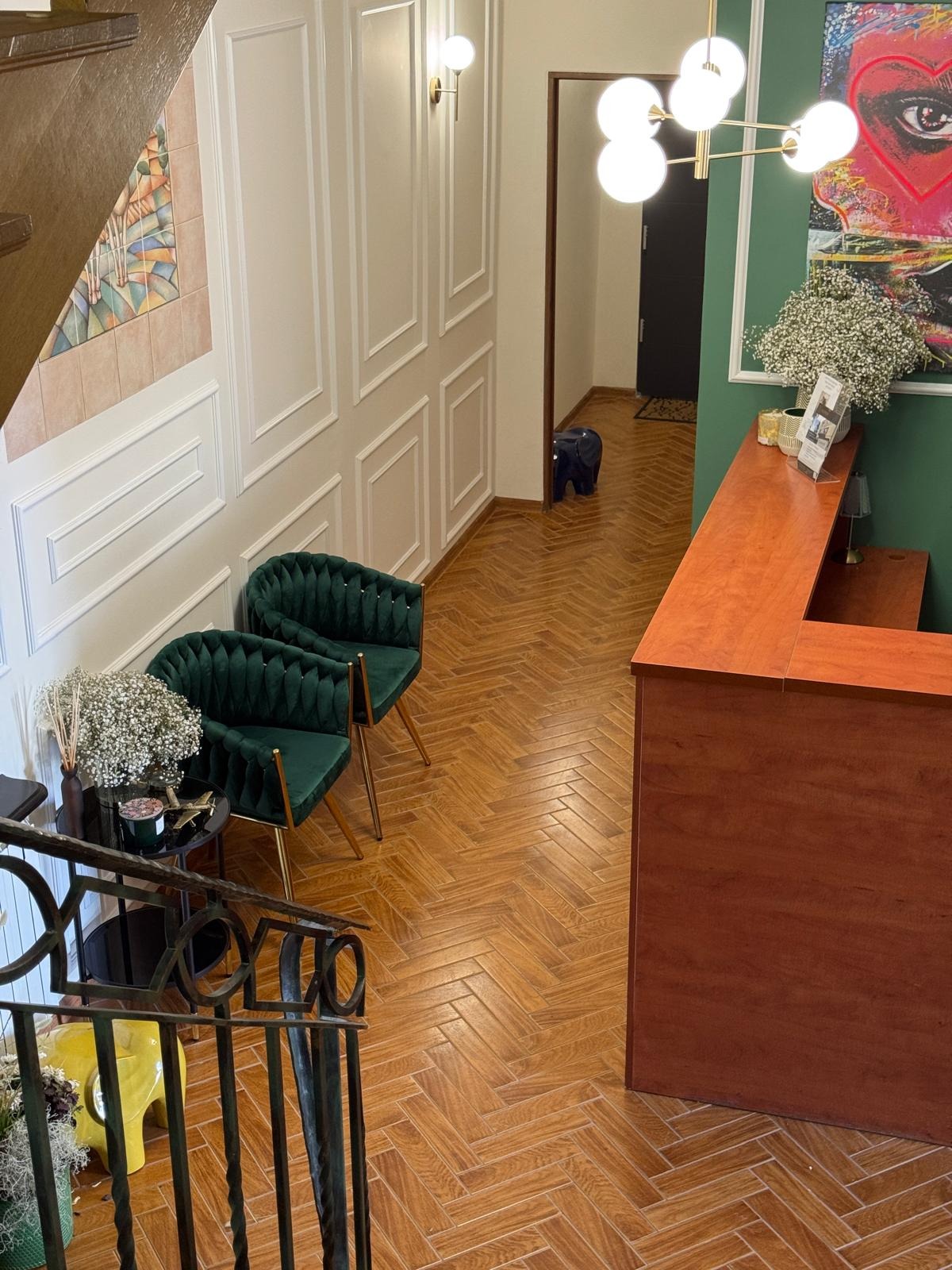 Eleganckie wnętrze biura z recepcją, zielonymi fotelami i parkietem w jodełkę. W tle dekoracje ścienne i oświetlenie. Widok z góry na hol.