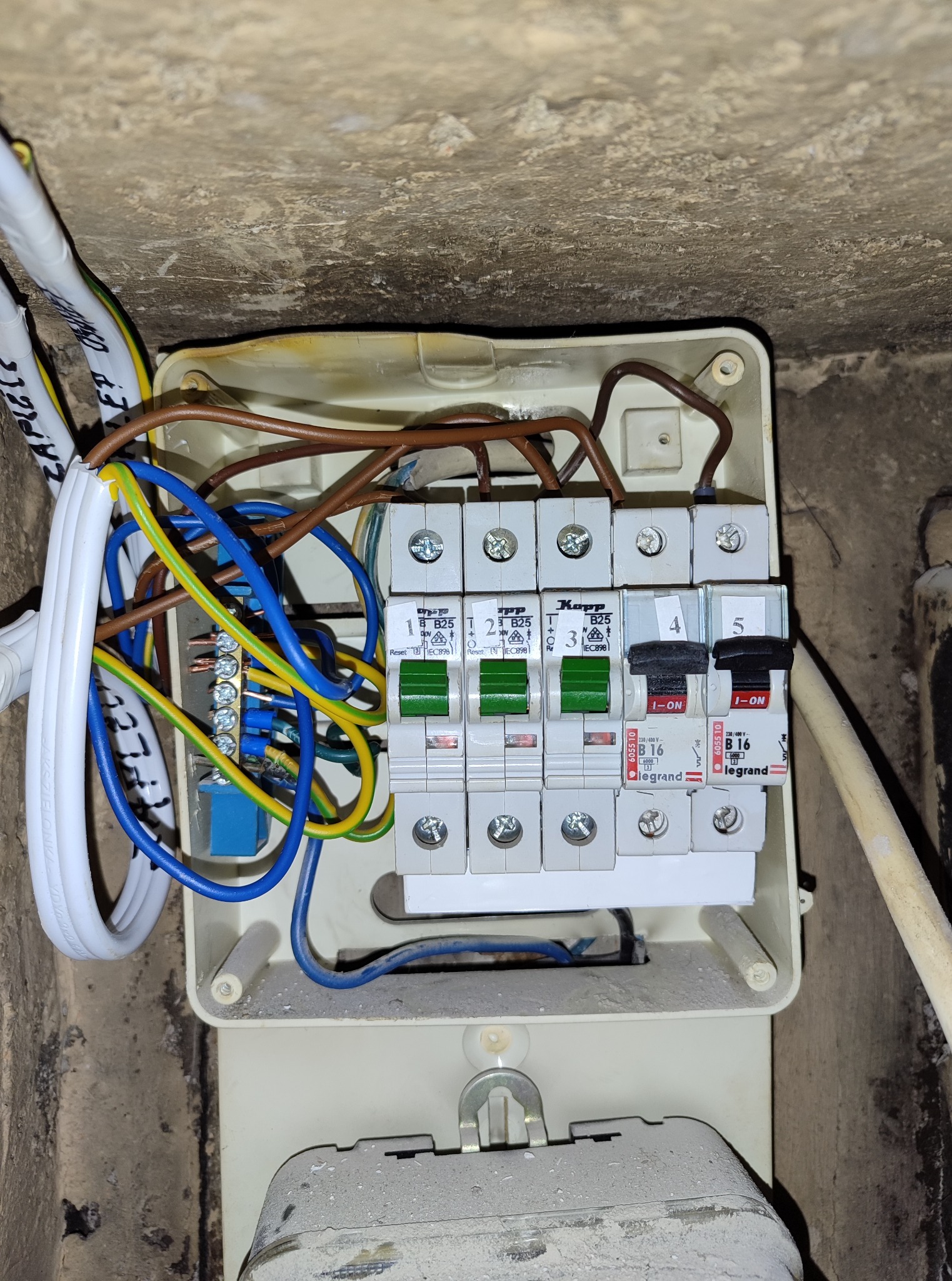 Rozdzielnica elektryczna w trakcie montażu: widoczne bezpieczniki, przewody i listwa zaciskowa w beżowej obudowie. Rozdzielone obwody oświetlenia i zasilania.