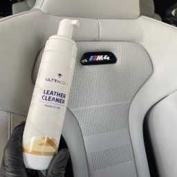 Perfect Clean Car detailing - Białe skórzane siedzenie M4 z perforacją, czyszczone preparatem Ultracoat Leather Cleaner, trzymanym w dłoni w czarnej rękawicy. Detailing wnętrza.