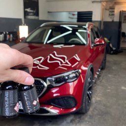 Perfect Clean Car detailing - Czerwony samochód po aplikacji powłoki ceramicznej, z widocznymi buteleczkami Skyline i Vista w dłoni. Detailing w dobrze oświetlonym garażu.
