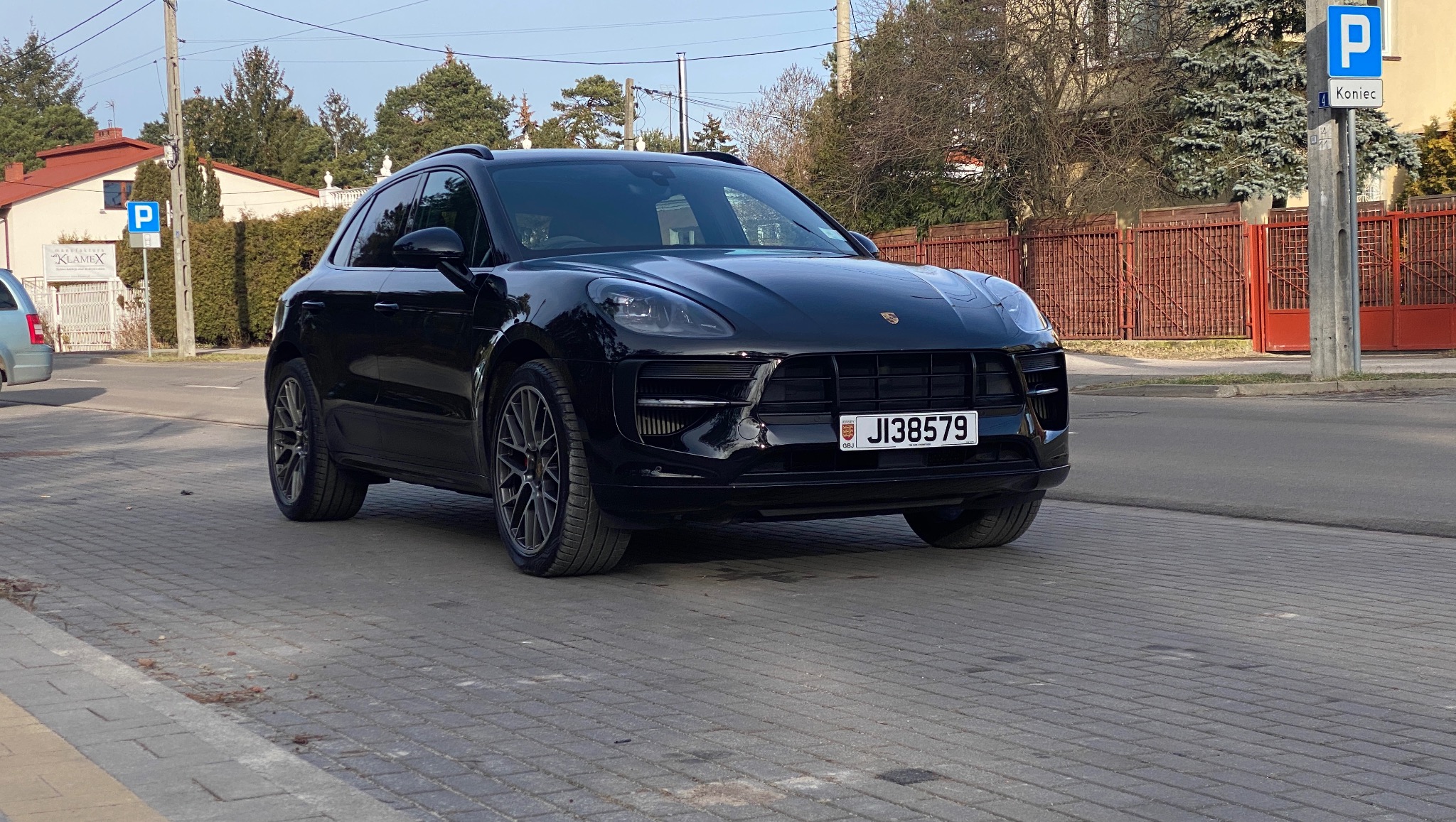 Czarny Porsche Macan, zaparkowany na chodniku z kostki brukowej, z widoczną tablicą rejestracyjną i elementami otoczenia miejskiego w tle.