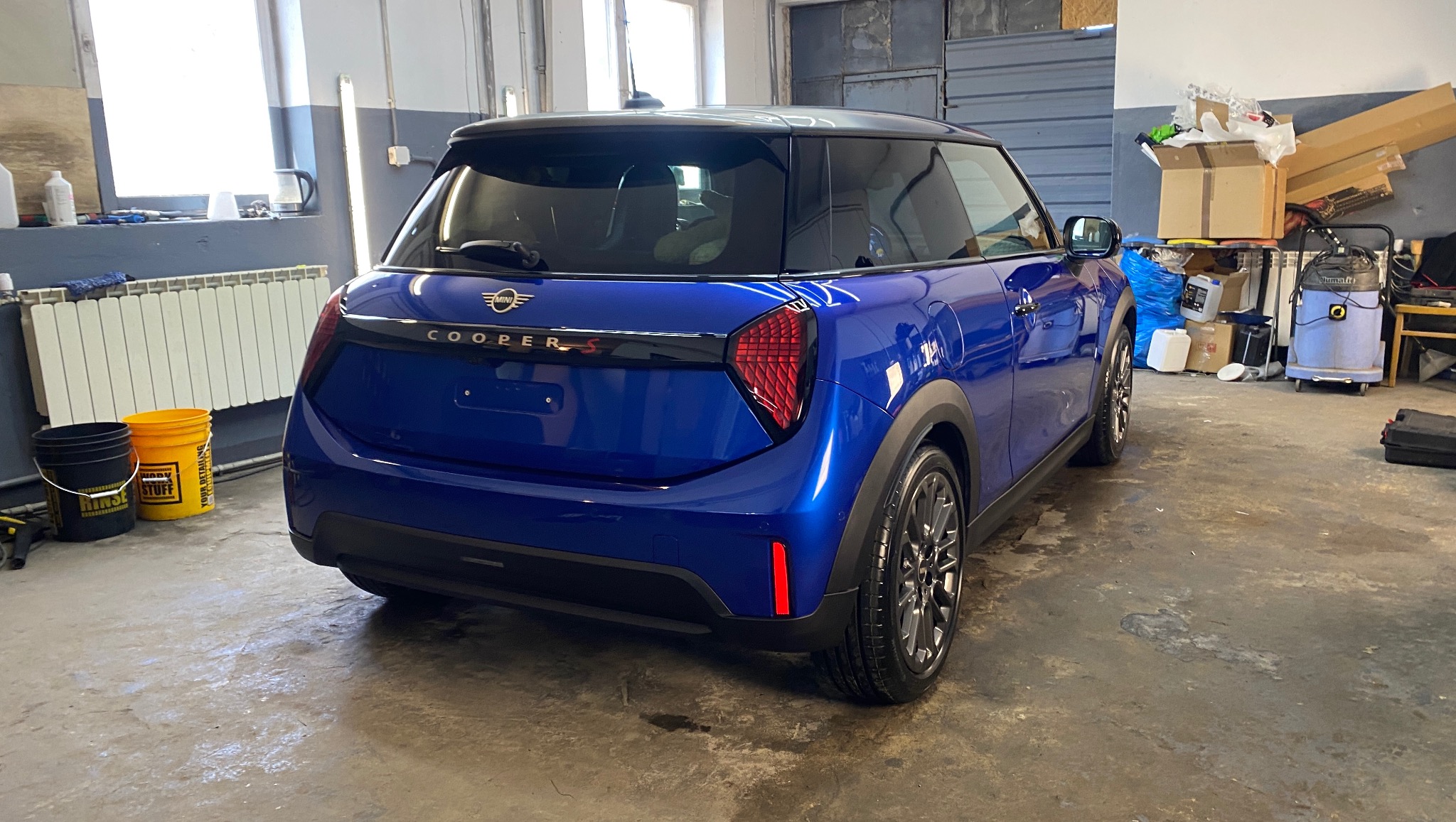 Błyszczący, niebieski Mini Cooper S po detailingu w warsztacie, widok z tyłu. Widoczne odblaski światła na lakierze i czyste felgi.