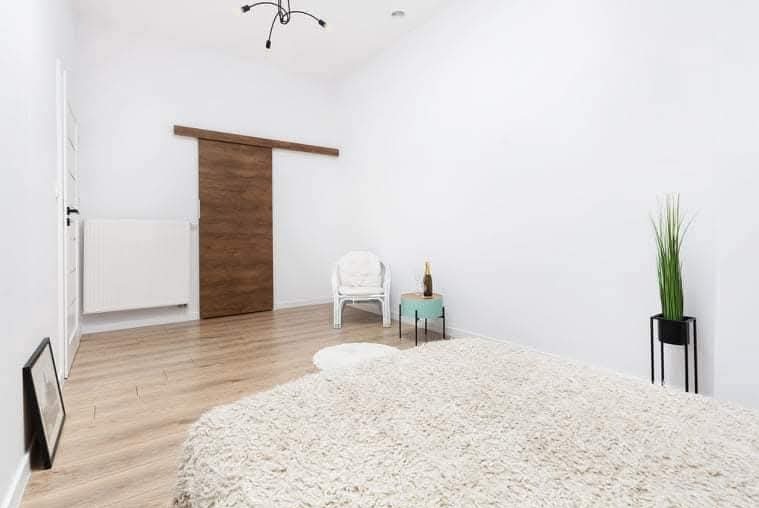 Jasne wnętrze pokoju z drewnianymi drzwiami przesuwnymi, białymi ścianami i puszystym dywanem. Minimalistyczny wystrój, lampa sufitowa o nowoczesnym designie.