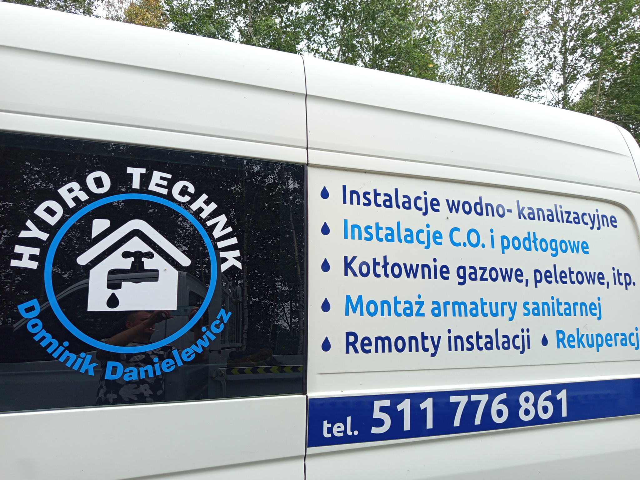Biały samochód dostawczy z reklamą firmy Hydro Technik Dominik Danielewicz, oferującej instalacje wodno-kanalizacyjne, C.O., kotłownie i montaż armatury sanitarnej.