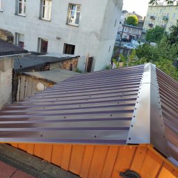 Twój Dach - Nowy, brązowy dach z blachy trapezowej z widocznymi śrubami i obróbką blacharską na tle budynków mieszkalnych i zieleni. Ujęcie z góry.