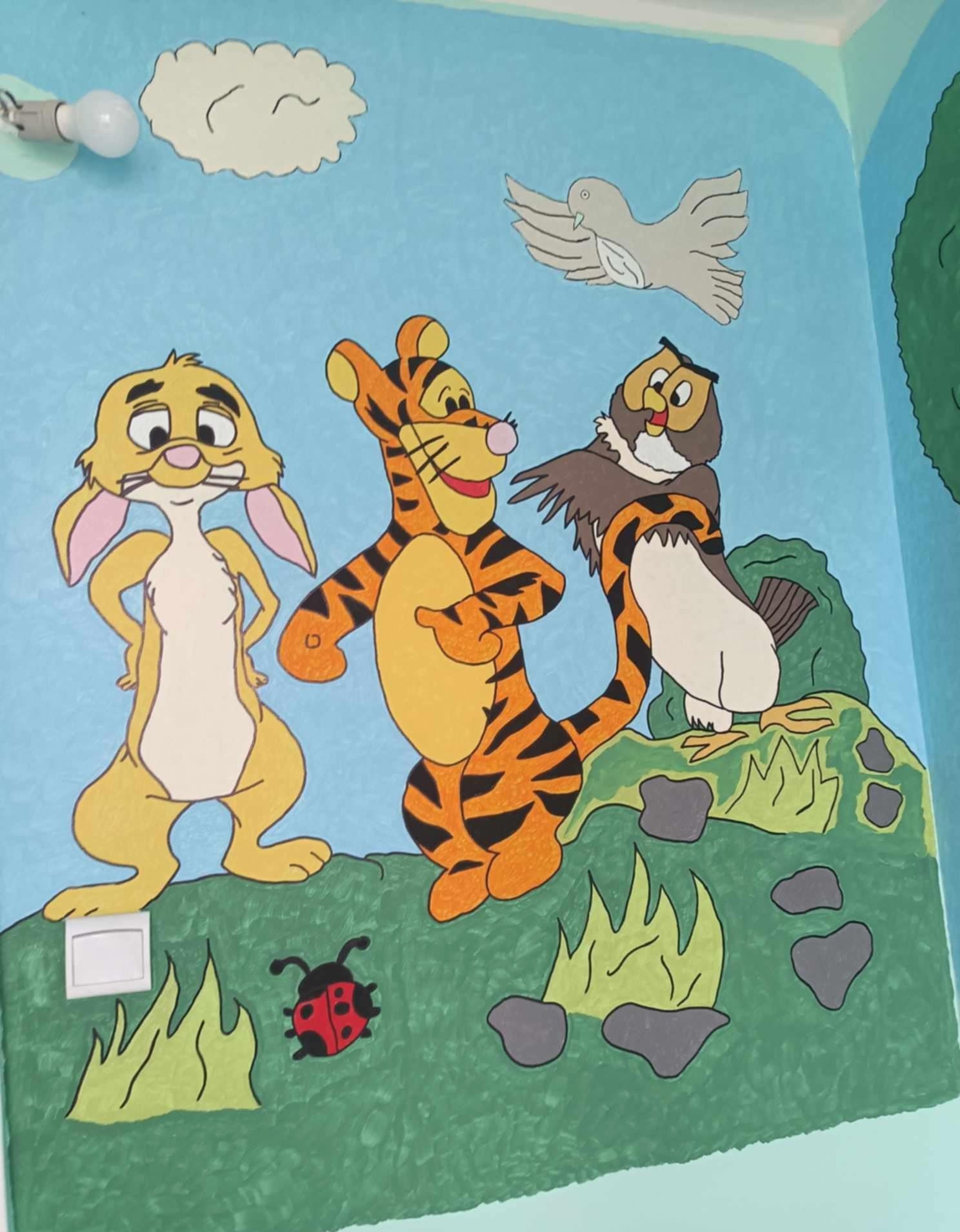 Ręcznie malowana ściana w Grudziądzu z postaciami z bajki: Królik, Tygrysek i Sowa na tle nieba i trawy. Dziecięcy motyw, jasne kolory, widoczna żarówka i włącznik.