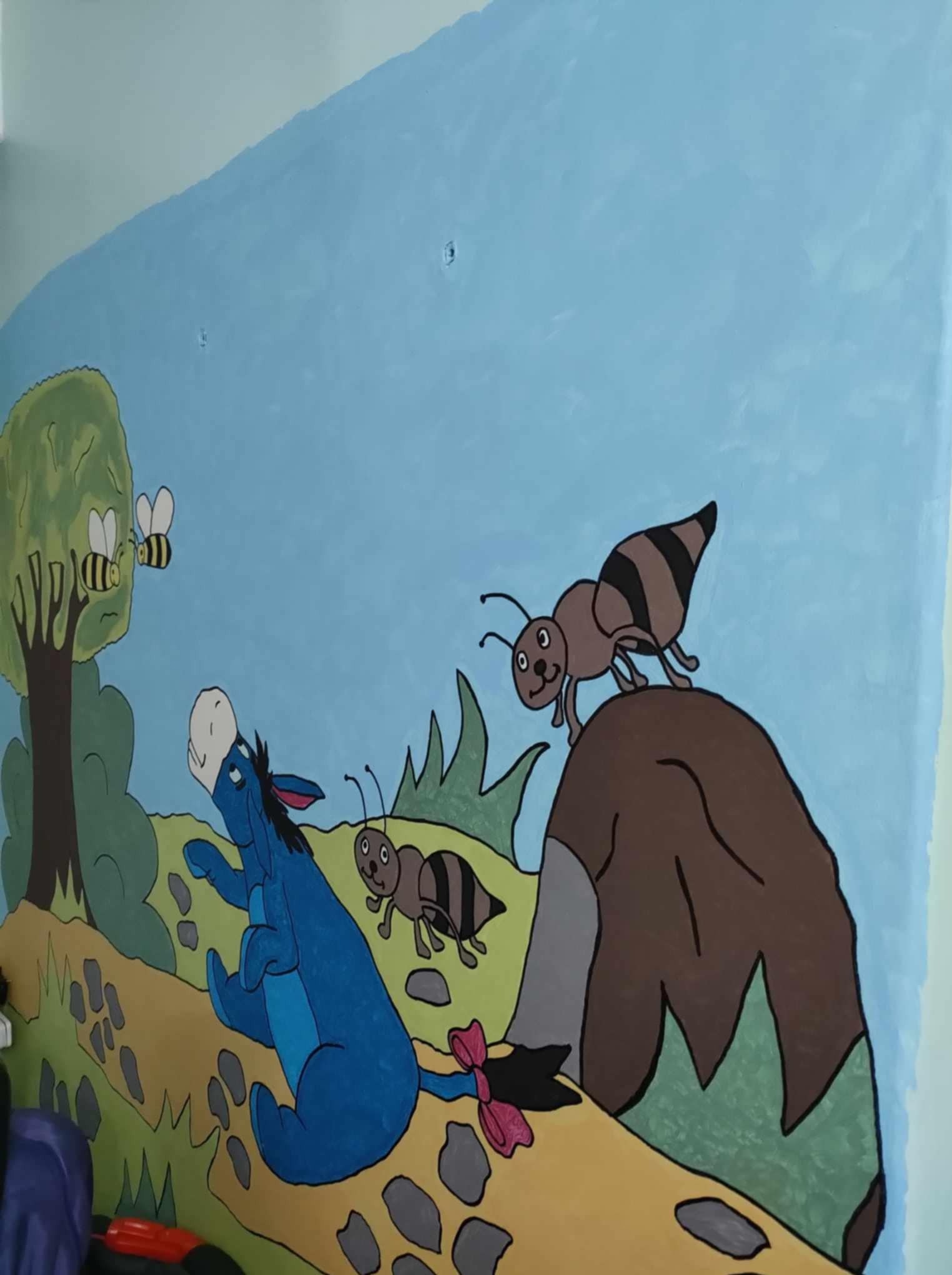 Malowidło ścienne w pokoju dziecięcym: osiołek, pszczoła, mrówki i drzewo na tle błękitnego nieba. Bajkowy motyw, ręcznie malowane postacie.