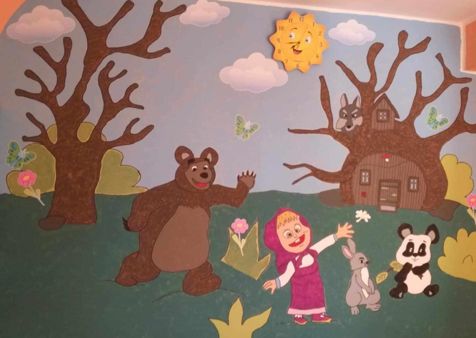 Malowidło ścienne w pokoju dziecięcym z motywami z bajki „Masza i Niedźwiedź”: niedźwiedź, Masza, wilk w domku na drzewie, panda, królik, zegar słońce i chmury.