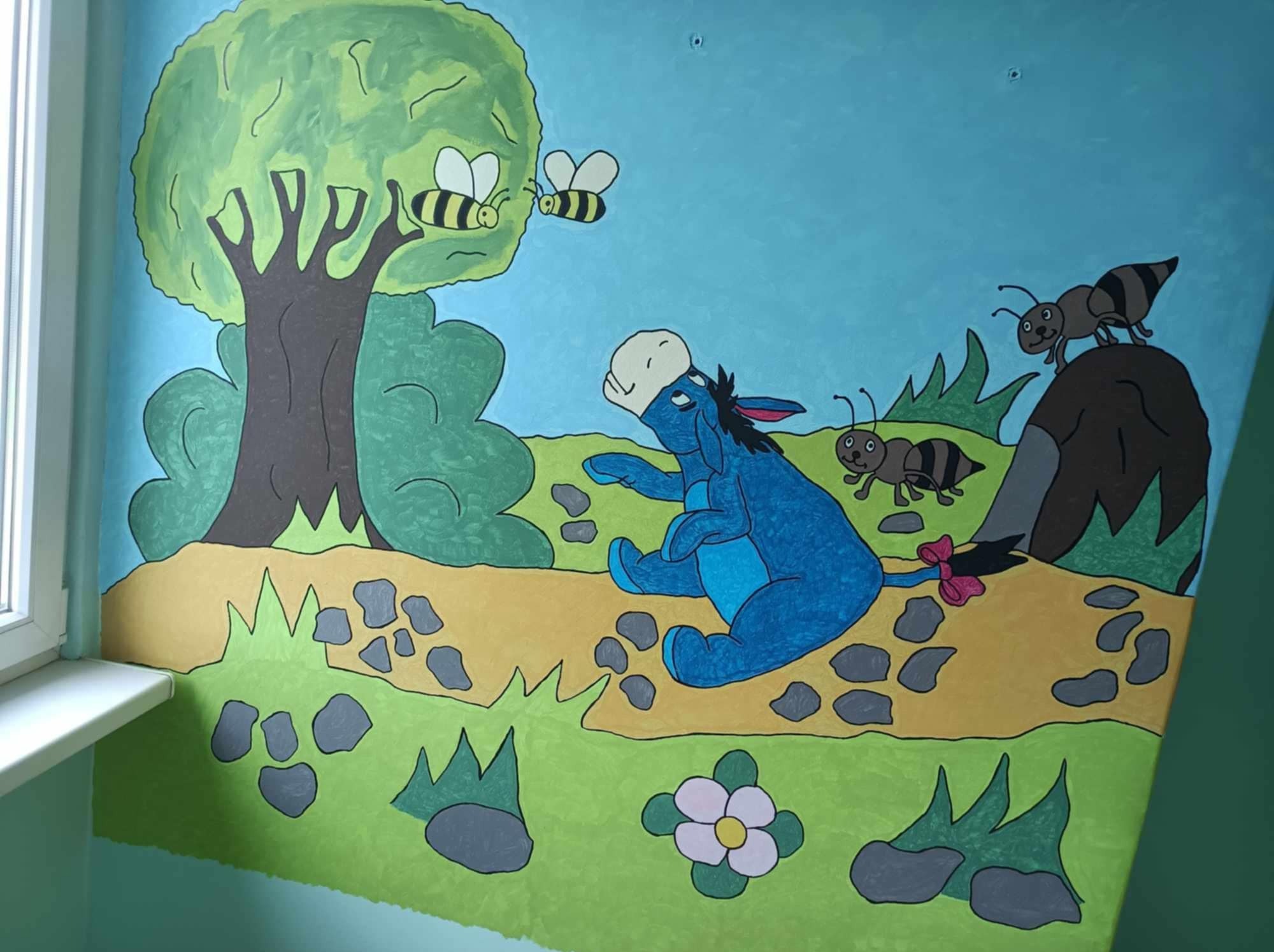Ręcznie malowana, bajkowa scena na ścianie z osiołkiem Kłapouchym, pszczołami i mrówkami w pokoju dziecięcym. Artystyczne malowanie ścian.