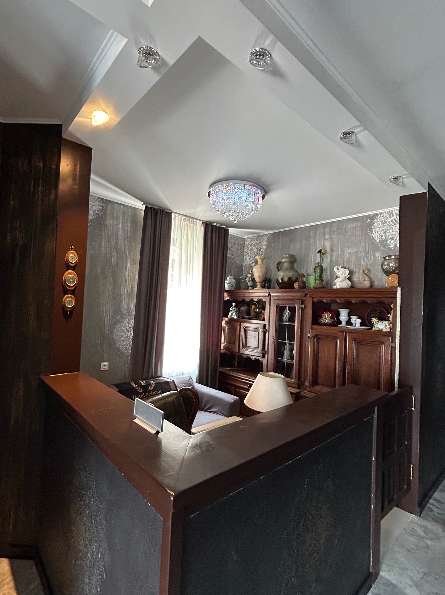 Eleganckie wnętrze z barkiem, dekoracyjną ścianą, kryształowym żyrandolem i klasycznymi meblami. Nietypowy kąt ujęcia podkreśla głębię pomieszczenia.