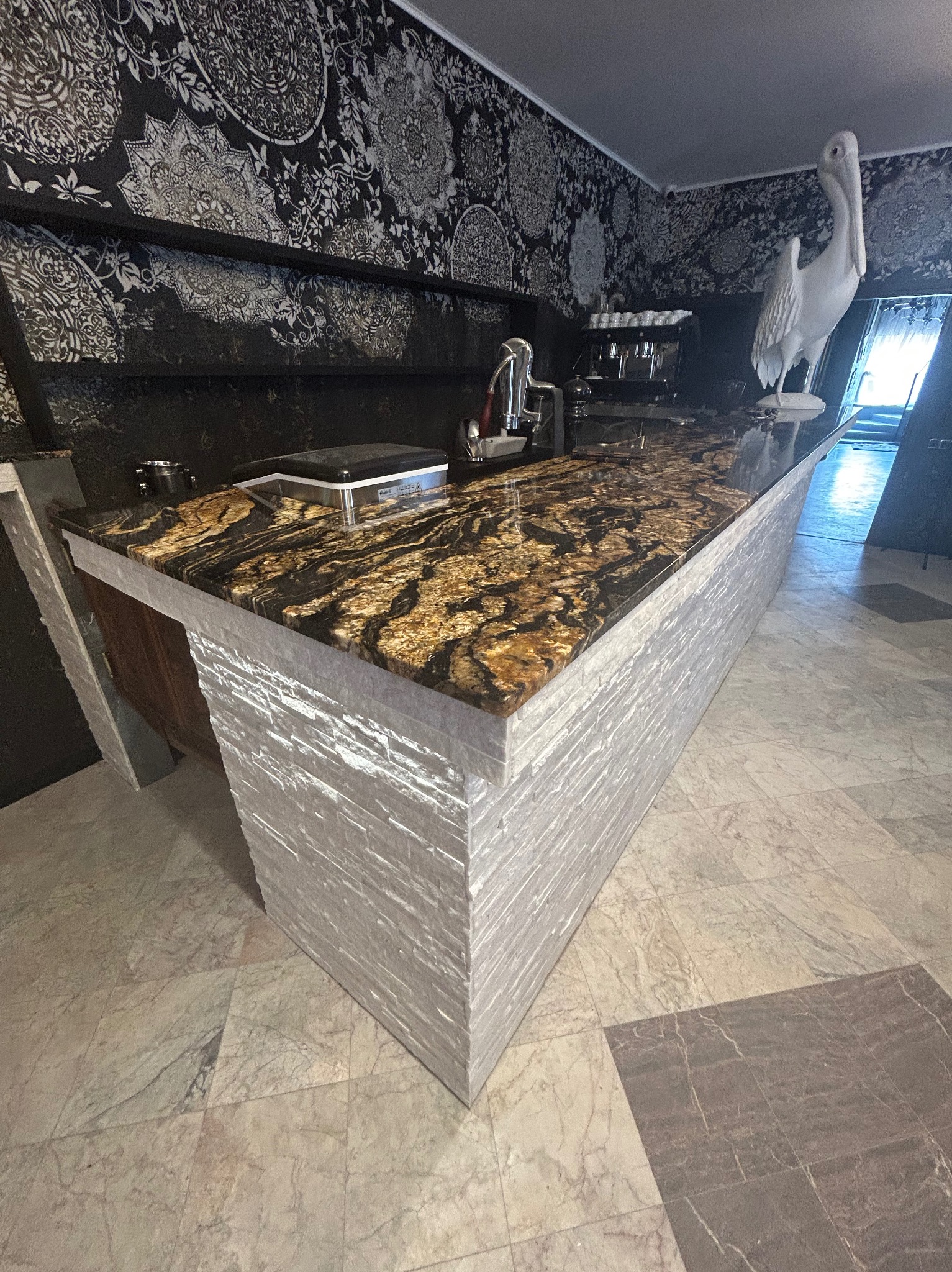 Wykończona wyspa kuchenna z blatem z kamienia i dekoracyjną okładziną w Kielcach. W tle wzorzysta tapeta i ozdobny pelikan.