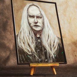 Epicdot - Portret olejny mężczyzny z długimi białymi włosami, w czarnej ramie, ustawiony na małej, drewnianej sztaludze na ciemnym tle. Widoczne ślady pędzla i faktura farby.