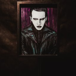 Epicdot - Portret w ramie, stylizowany na Marilyn Mansona, z białym makijażem i czarną skórzaną kurtką, na ciemnym tle. Wyraziste, ciemne oczy i usta.