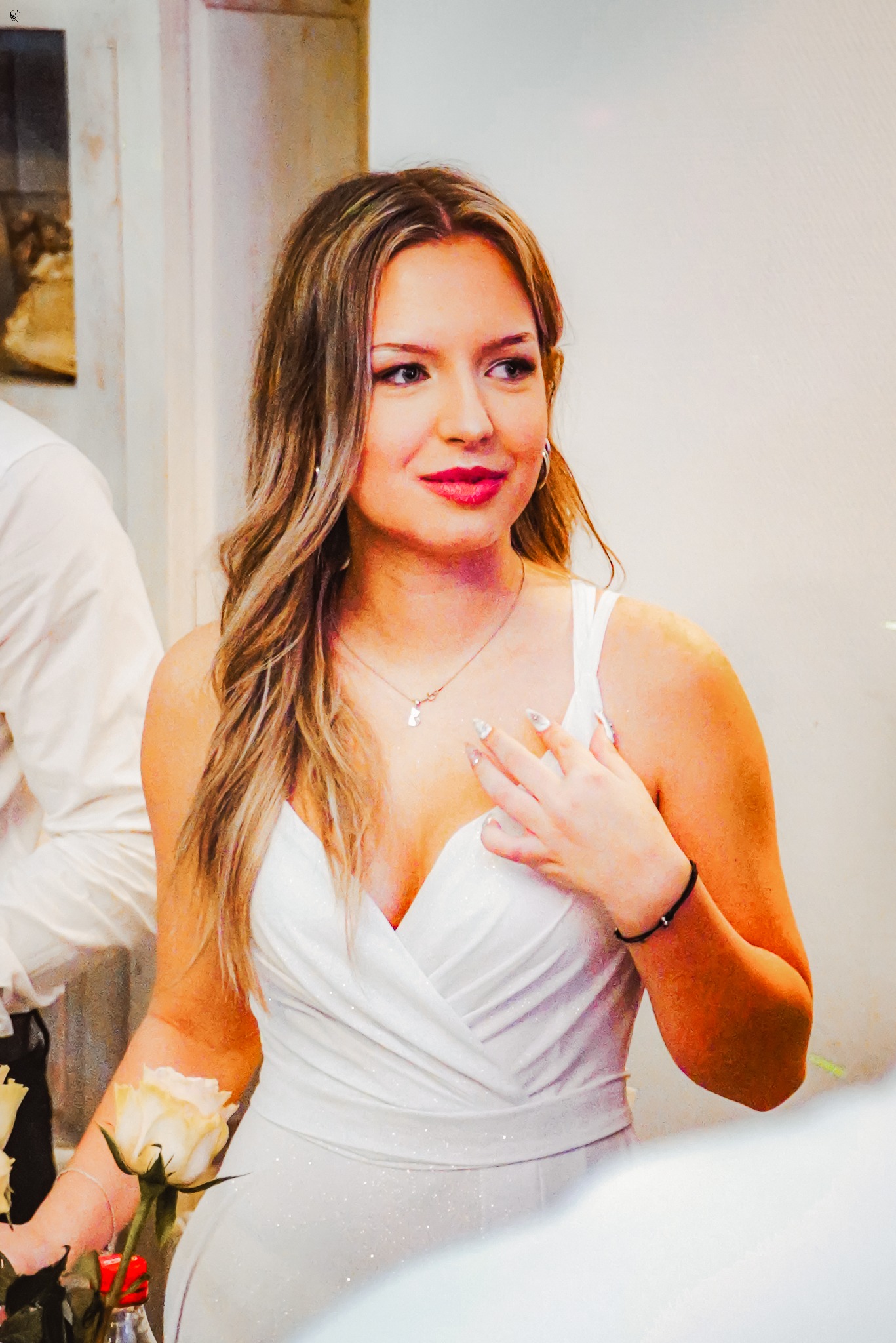 Portret kobiety w białej sukni, z delikatnym makijażem i blond włosami, trzymającej białą różę. Ujęcie z bliska, skupione na twarzy i górnej części ciała.