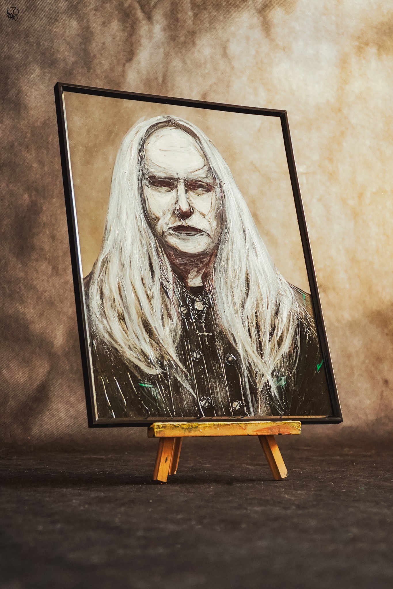 Portret olejny mężczyzny z długimi białymi włosami, w czarnej ramie, ustawiony na małej, drewnianej sztaludze na ciemnym tle. Widoczne ślady pędzla i faktura farby.