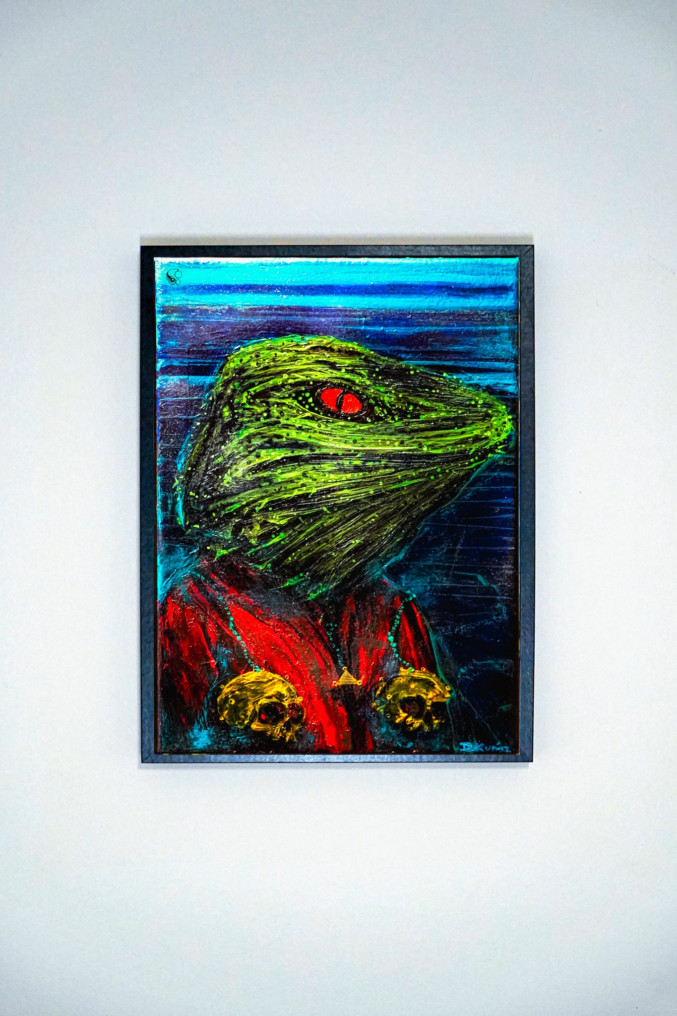 Oprawiony obraz przedstawia abstrakcyjną postać z zieloną głową, czerwonymi oczami i czerwono-złotym strojem na tle niebiesko-czarnych pociągnięć pędzla. Widoczne faktury farby.