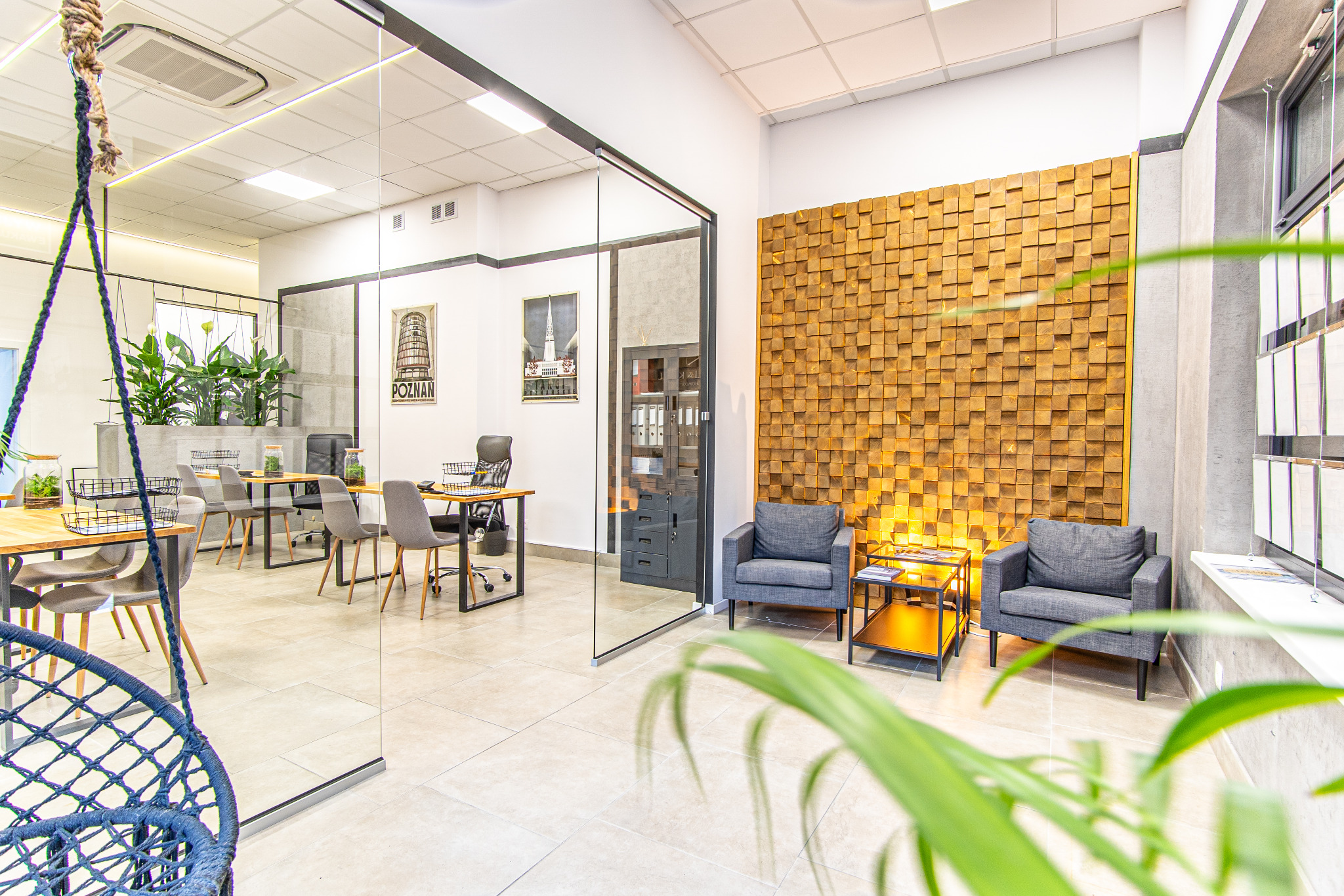 Nowoczesne biuro nieruchomości z dekoracyjną ścianą z drewna, szklaną ścianą działową i huśtawką brazylijską. Widoczne plakaty z motywami miejskimi.