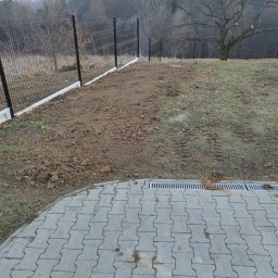 Firma Usługowa M-Bud Jakub Murzyn - Nowoczesne ogrodzenie panelowe z podmurówką na nierównym terenie. Widoczna kostka brukowa i drenaż liniowy. W tle drzewa bez liści i lekka mgła.
