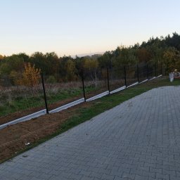 Firma Usługowa M-Bud Jakub Murzyn - Nowoczesne ogrodzenie panelowe z podmurówką betonową, widoczne na tle zieleni i kostki brukowej. Minimalistyczny design, czarne słupki, szara podmurówka.