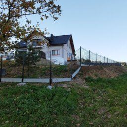 Firma Usługowa M-Bud Jakub Murzyn - Nowoczesne ogrodzenie panelowe z podmurówką, zainstalowane na nierównym terenie działki z widokiem na dom jednorodzinny. Jesienne drzewo w lewym górnym rogu kadru.