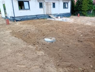 Przygotowany teren pod budowę z widocznym włazem kanalizacyjnym i fundamentami zabezpieczonymi folią. Ujęcie z poziomu gruntu.