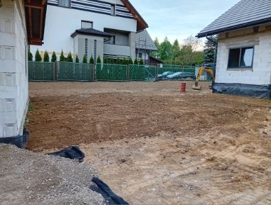 Przygotowany teren pod budowę w Gruszowie, z widoczną mini koparką i ogrodzeniem. Częściowo wykopana ziemia, gotowa pod fundamenty.
