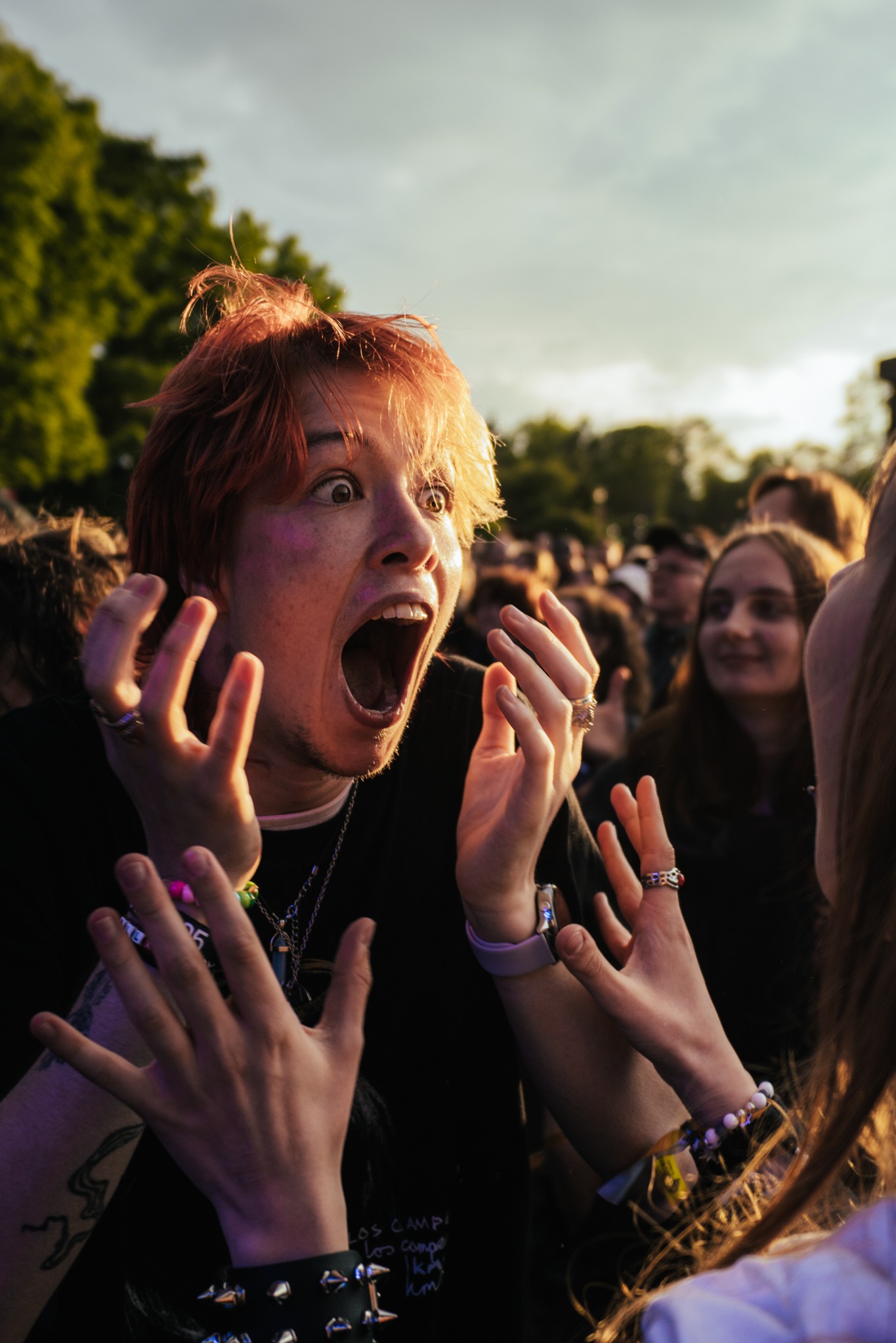 Ekspresyjny portret młodego mężczyzny z otwartymi ustami na tle rozmytego tłumu podczas wydarzenia plenerowego, uchwycony w dynamicznym ujęciu.