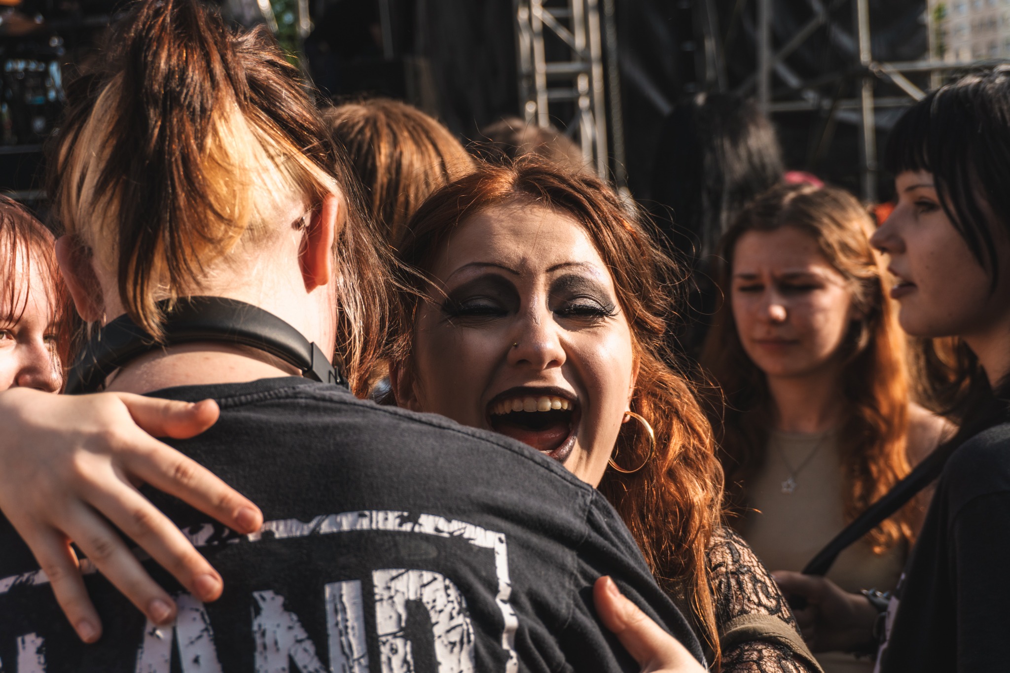 Rozemocjonowana, radosna kobieta z rudymi włosami, w tłumie, obejmująca kogoś w czarnej koszulce na tle sceny podczas koncertu.