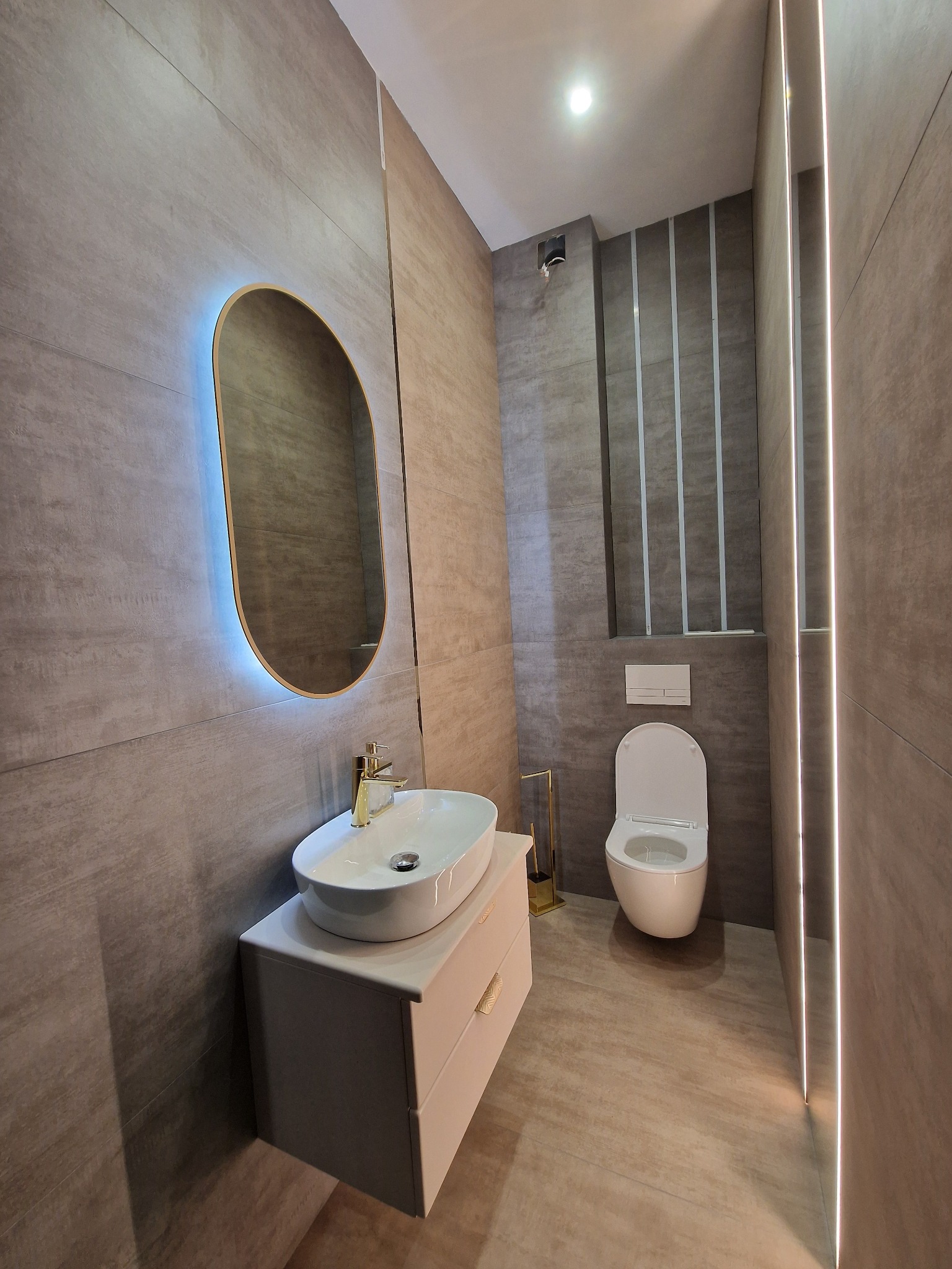 Nowoczesna łazienka w szarościach z podświetlanym lustrem, umywalką nablatową i toaletą. Minimalistyczny design, płytki imitujące kamień.