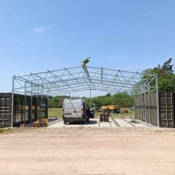 Ases sp zoo - Konstrukcja metalowa z kontenerami po bokach, prawdopodobnie w trakcie budowy, na zewnątrz, w tle widoczny samochód dostawczy i drzewa.