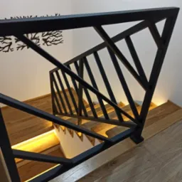 Nowoczesna, czarna balustrada schodowa z geometrycznym wzorem i drewnianymi schodami z podświetleniem LED, widziana z góry pod kątem. Minimalistyczny design.