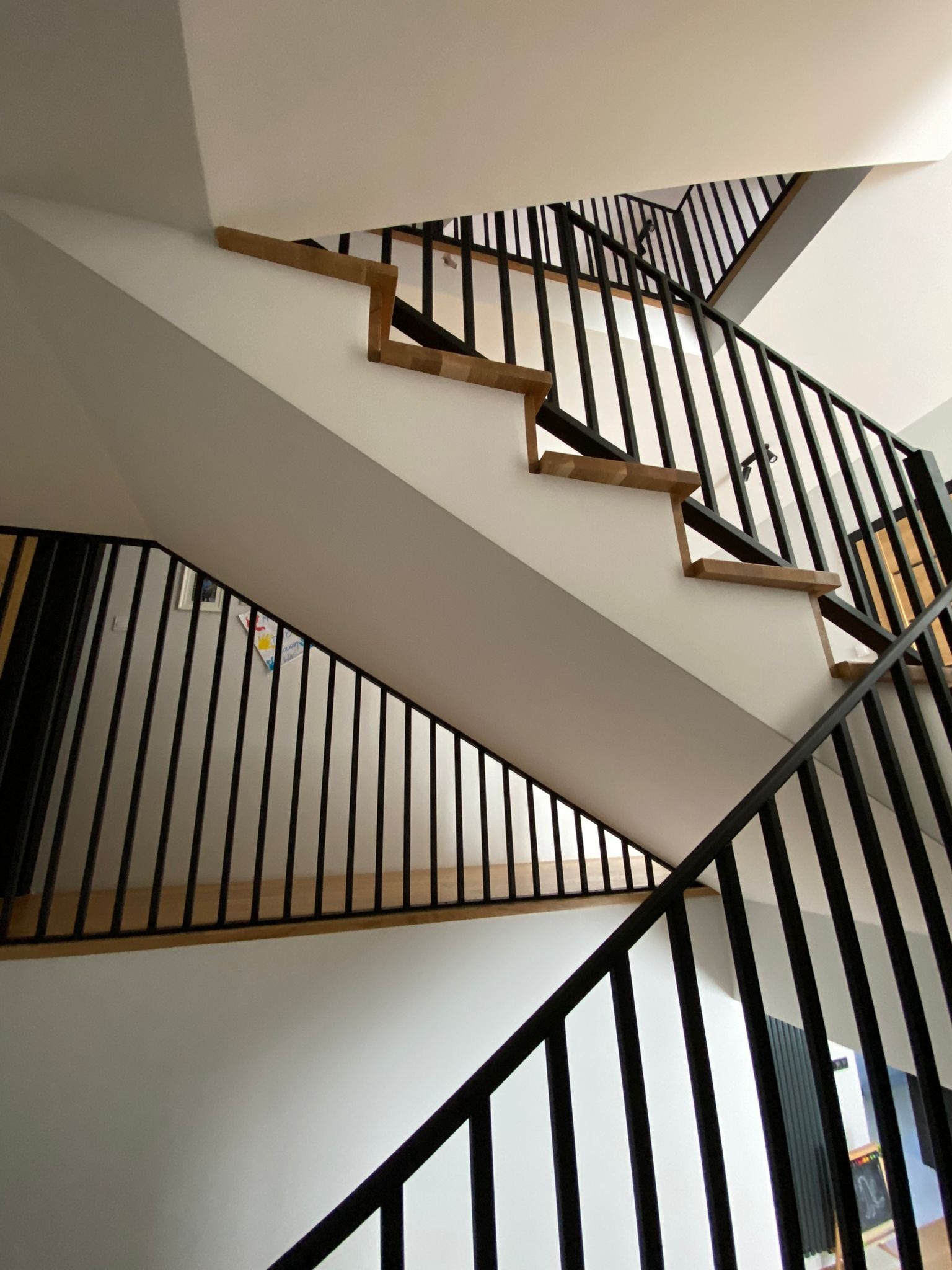 Wnętrze domu: schody drewniane z czarną, metalową balustradą, widok z dołu. Minimalistyczny design, białe ściany, nowoczesne wykończenie.