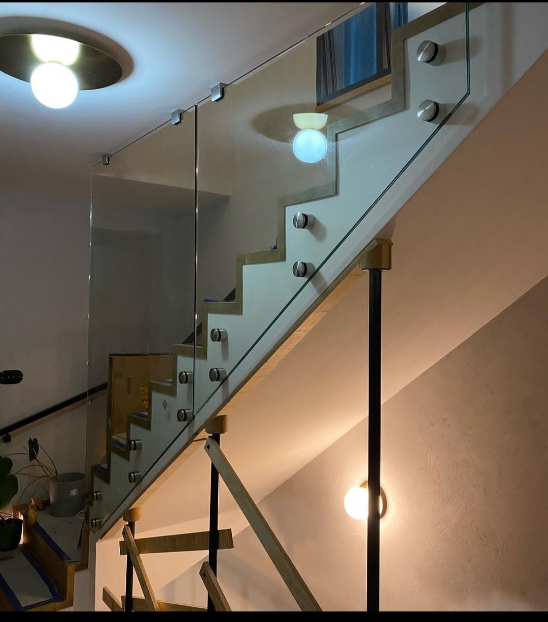 Nowoczesne schody z balustradą szklaną, mocowaną punktowo. Realizacja z Góry Kalwarii. Widoczne oświetlenie schodowe i elementy konstrukcyjne.