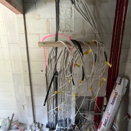 Daniel Krzyston - Surowa instalacja elektryczna w trakcie montażu w nowym budynku. Widoczne kable oznaczone żółtymi etykietami, prowadzone wzdłuż ściany z betonu komórkowego.