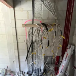 Surowa instalacja elektryczna w trakcie montażu w nowym budynku. Widoczne kable oznaczone żółtymi etykietami, prowadzone wzdłuż ściany z betonu komórkowego.