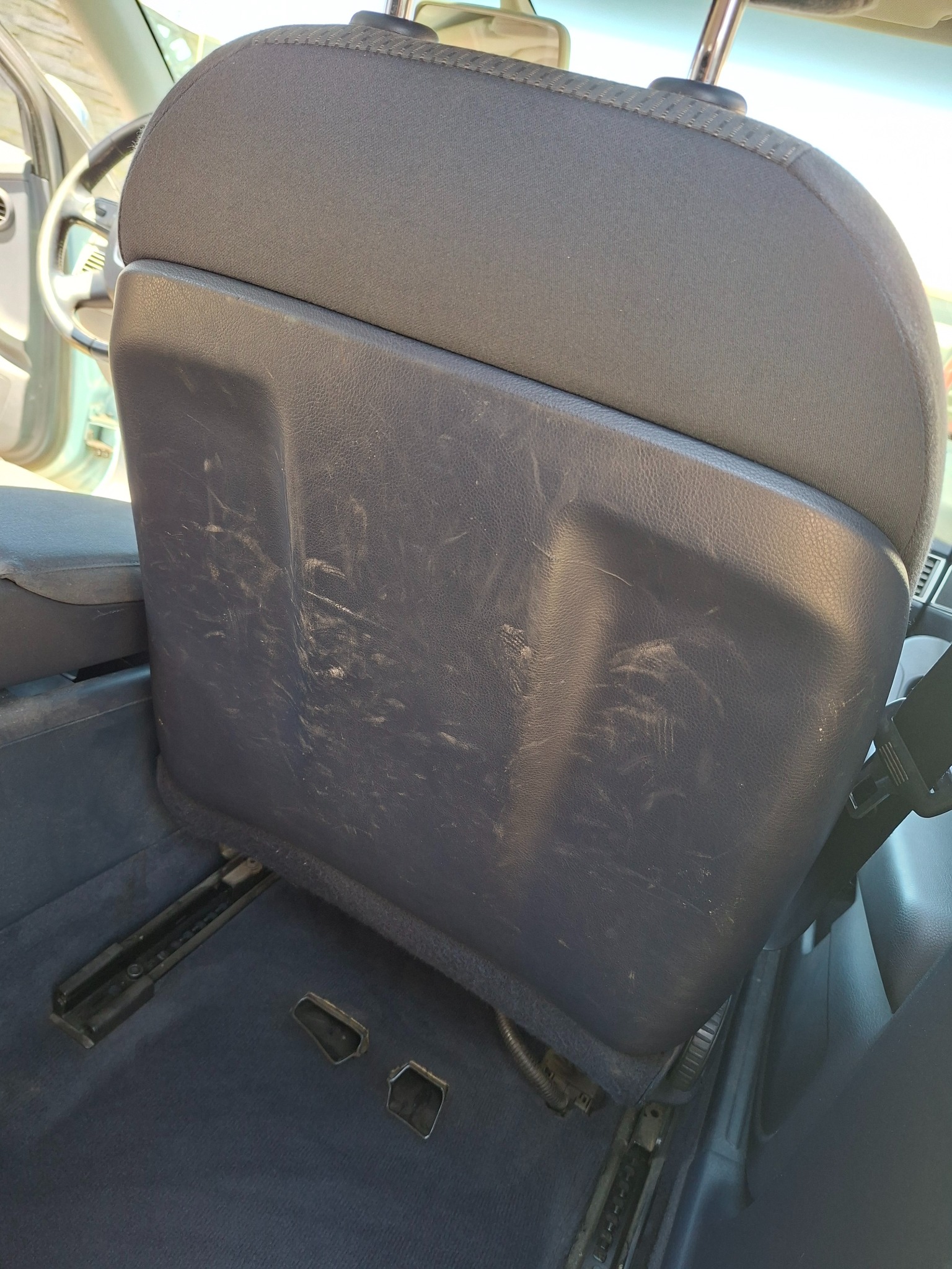 Zabrudzone, szare oparcie tylnego siedzenia samochodowego z widocznymi śladami użytkowania i plamami, wnętrze pojazdu.