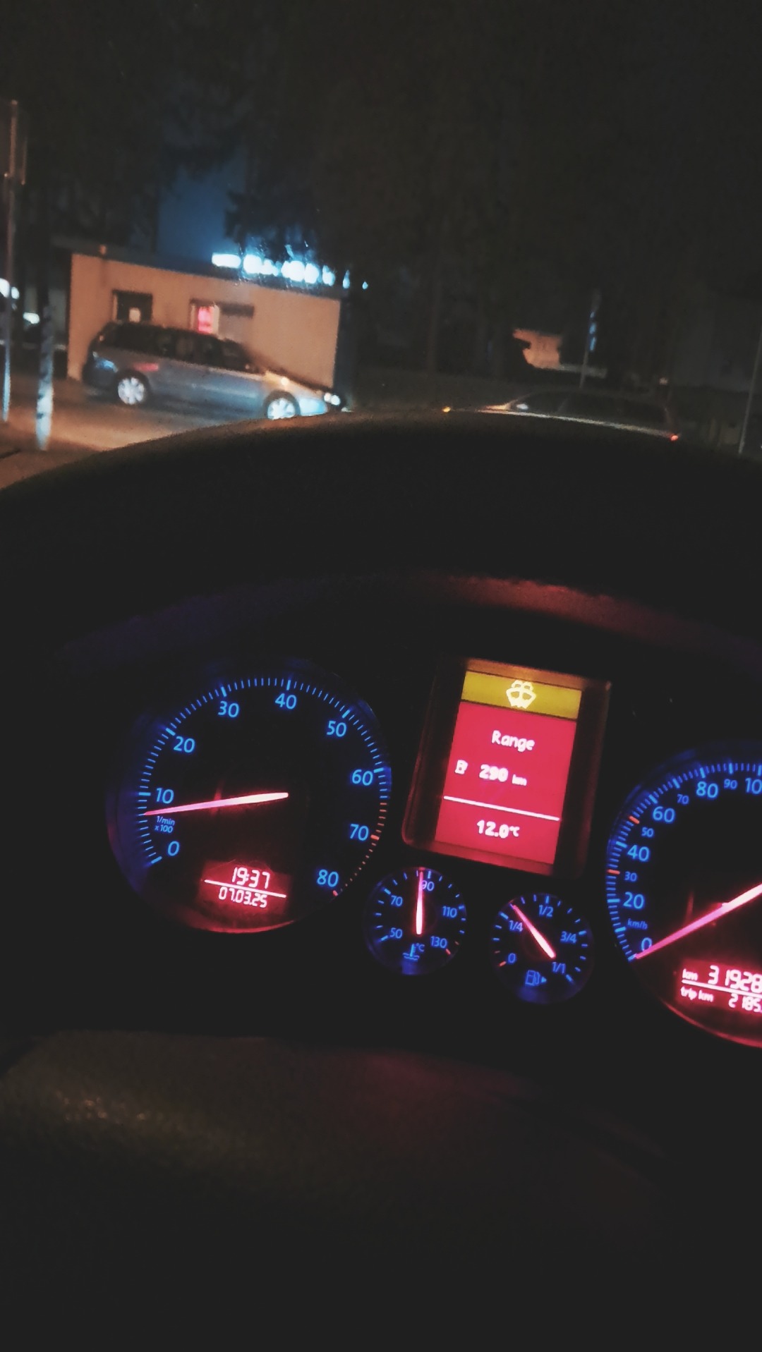 Deska rozdzielcza samochodu z podświetlonymi wskaźnikami w nocnym otoczeniu. Widoczny ekran z informacjami o zasięgu i temperaturze.