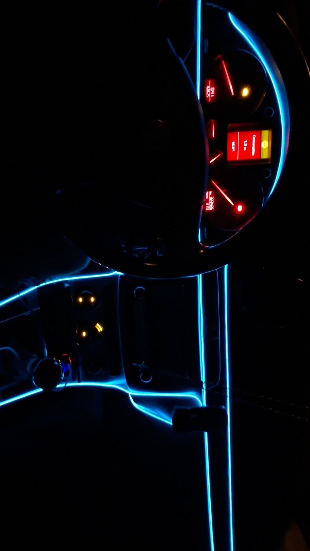 Deska rozdzielcza auta z niebieskim oświetleniem LED, widoczne zegary i kierownica w ciemnym wnętrzu pojazdu, światła tworzą futurystyczny efekt.