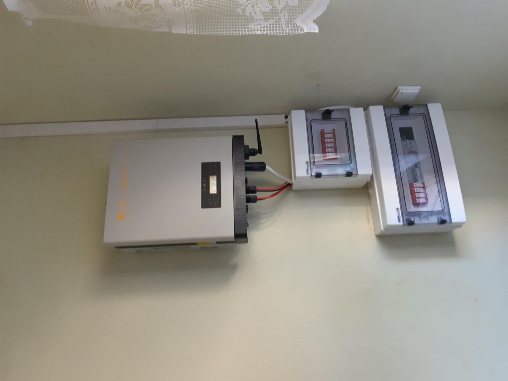 Zamontowany inwerter fotowoltaiczny z widocznymi zabezpieczeniami na ścianie wewnątrz budynku. Widoczne kable i elementy instalacji elektrycznej.