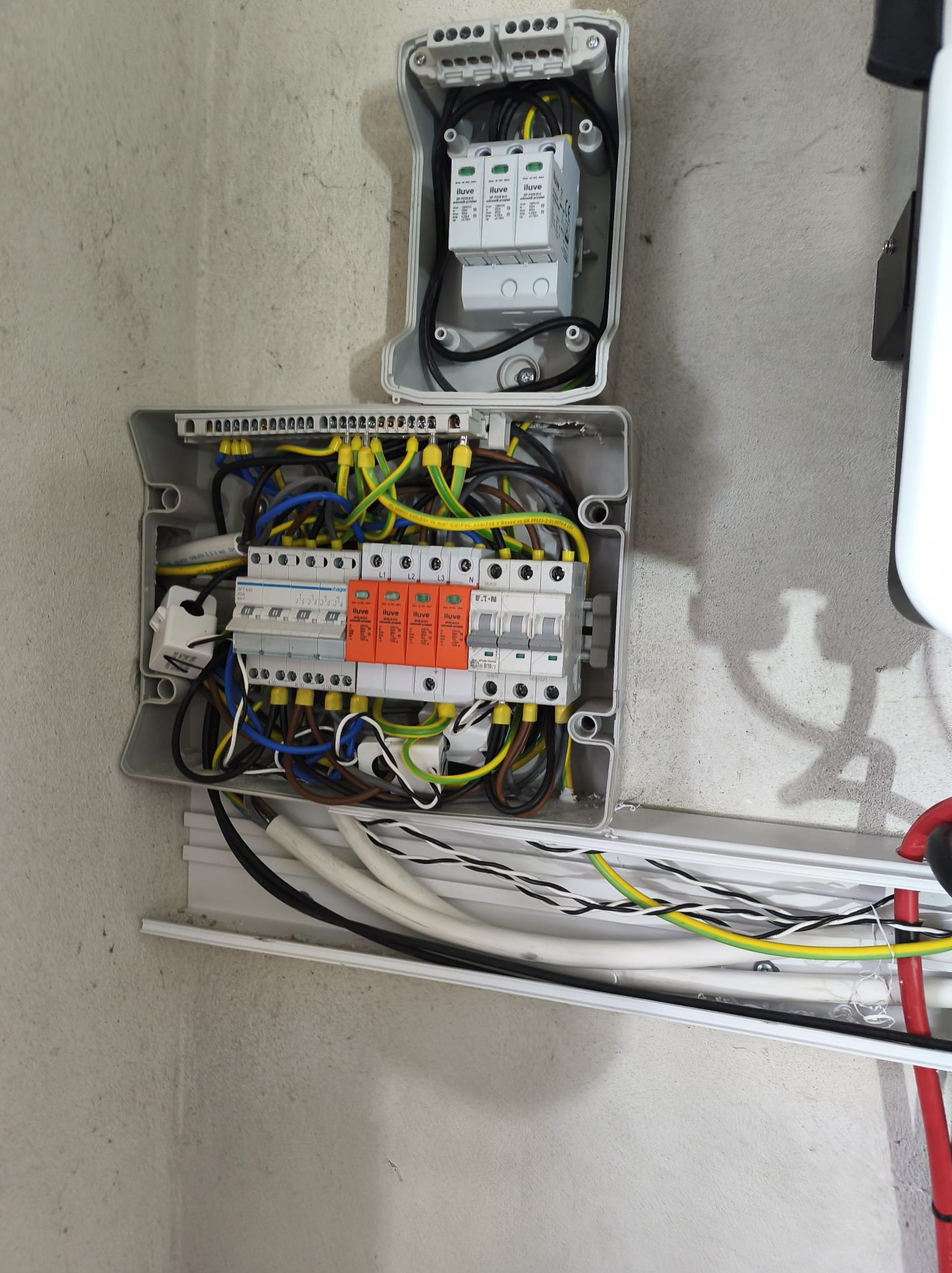 Otwarta skrzynka elektryczna z bezpiecznikami i przewodami na szarej ścianie, instalacja elektryczna zabezpieczeń przepięciowych w systemie OZE.