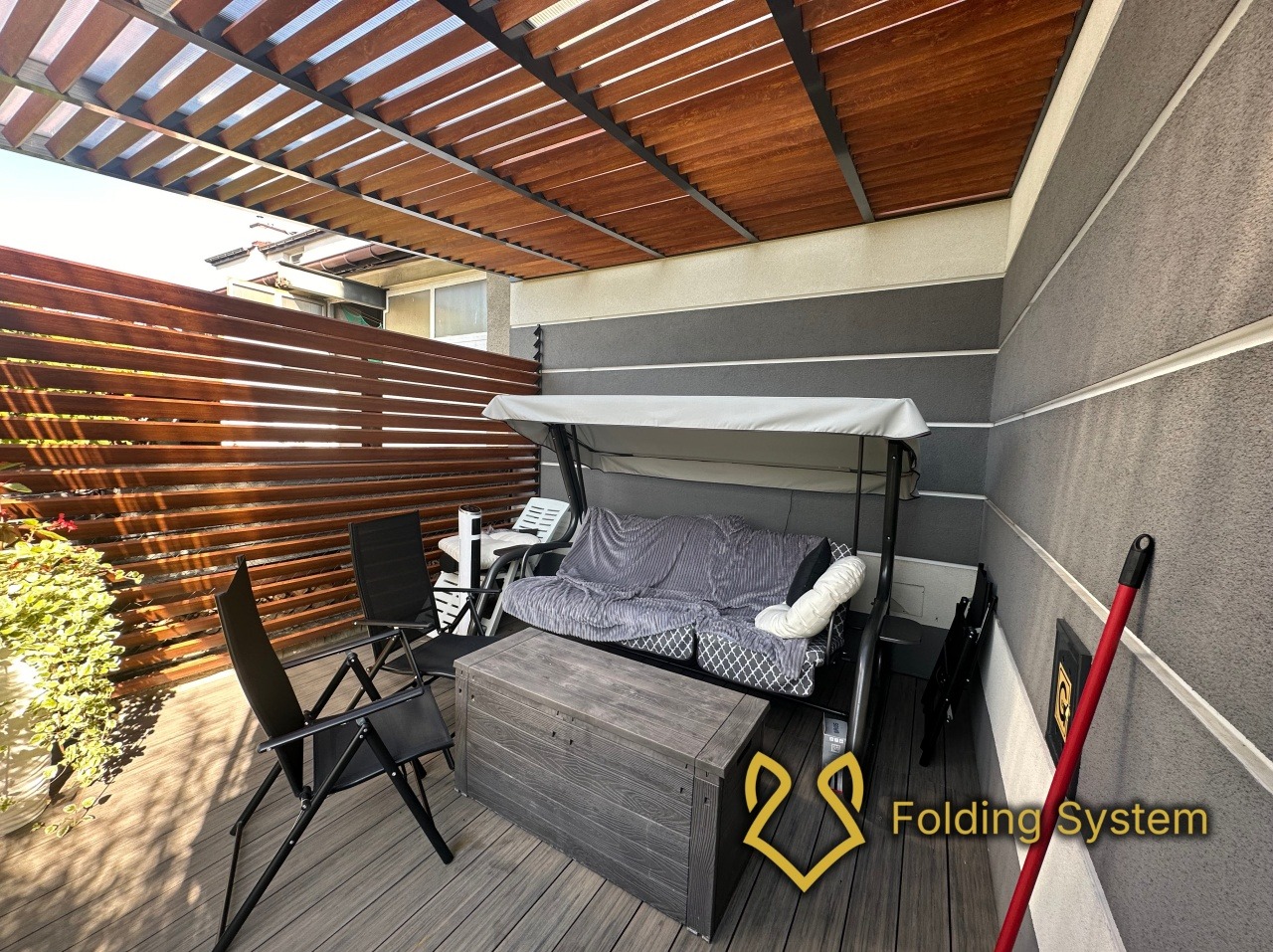 Zadaszony taras z drewnianą pergolą, huśtawką ogrodową i meblami. Kompozytowa deska tarasowa i drewniane panele zapewniają prywatność.