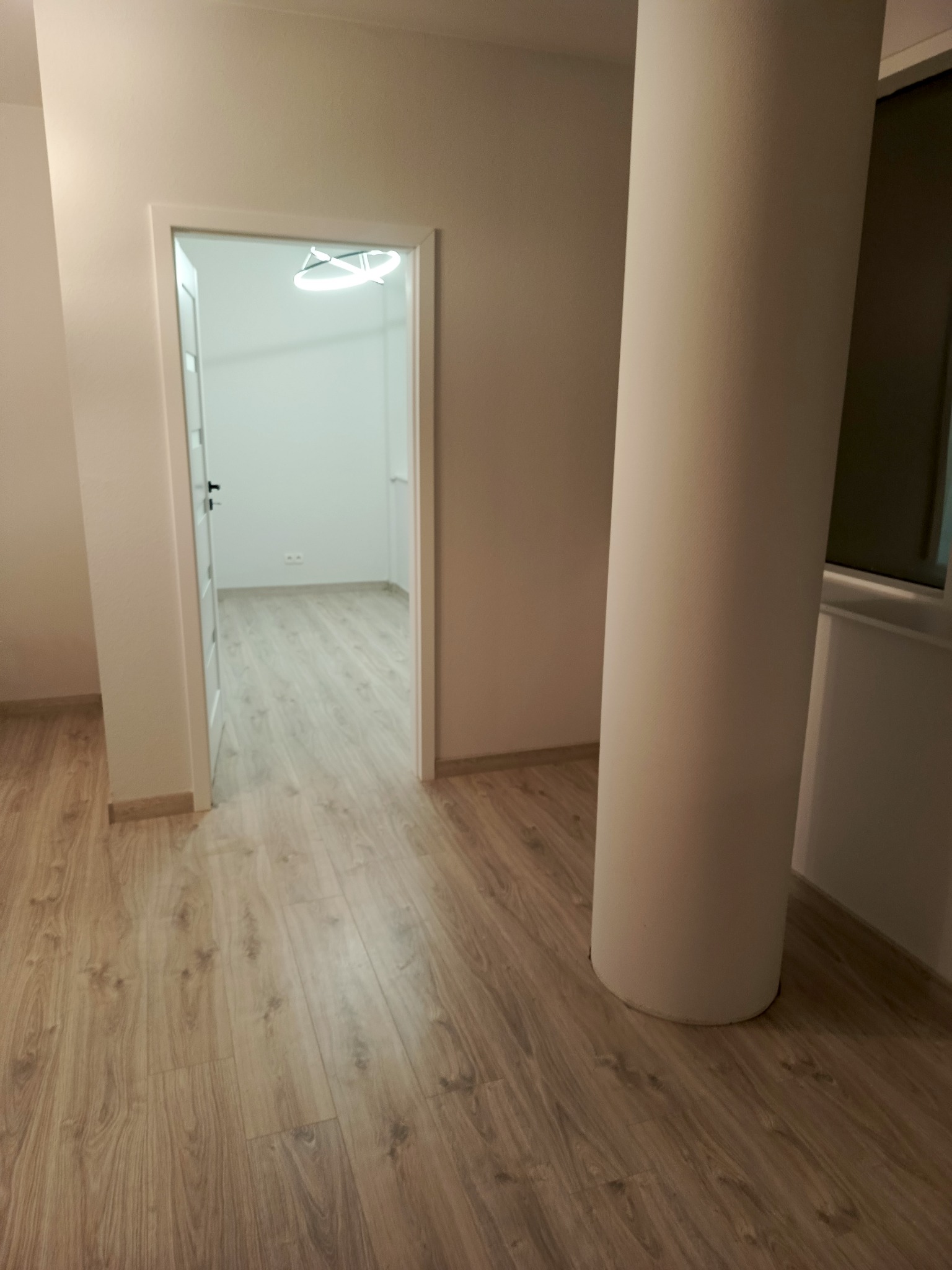 Jasne panele podłogowe w nowym wnętrzu z kolumną i otwartymi drzwiami do kolejnego pomieszczenia z nowoczesnym oświetleniem sufitowym.