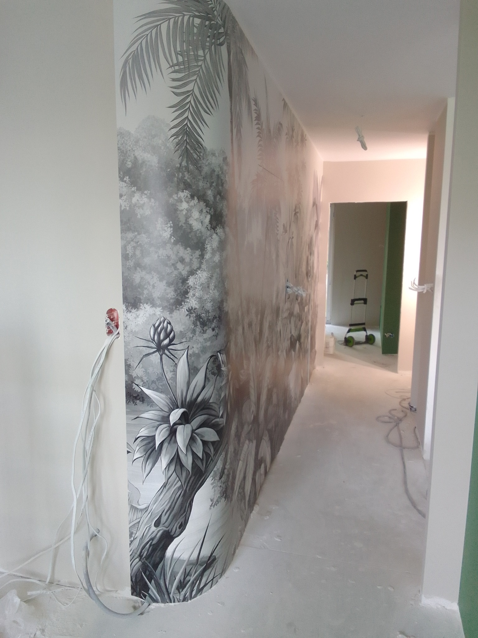 Korytarz w trakcie wykańczania z fototapetą w motywy roślinne. Widoczne przewody elektryczne i drabina w tle. Realizacja z dbałością o detale.